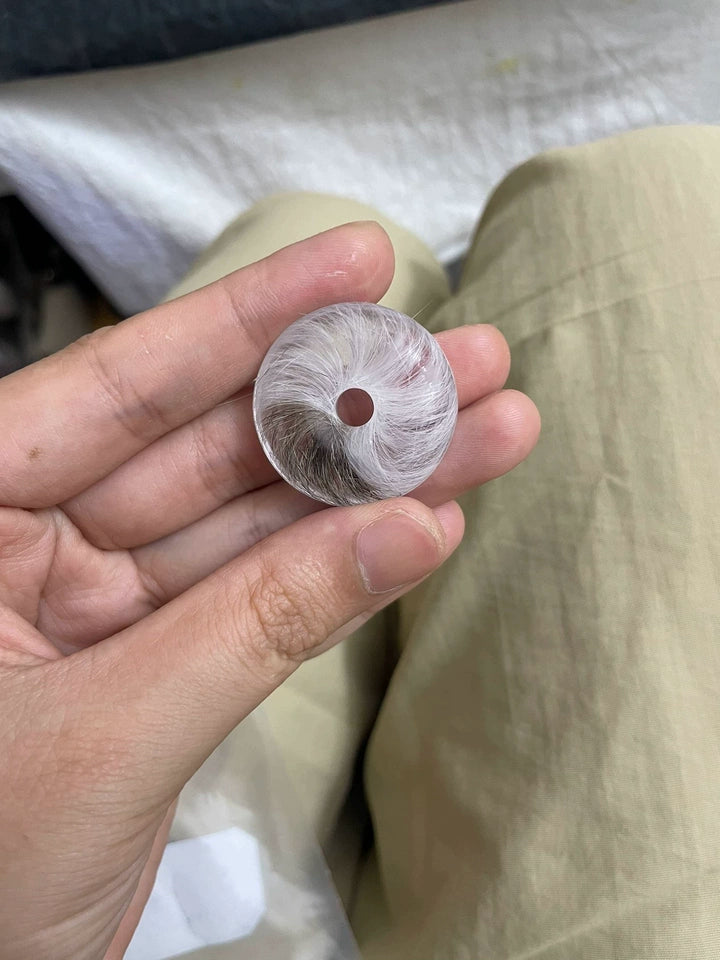 Hand holding a clear round keepsake with softly arranged grey and white pet fur