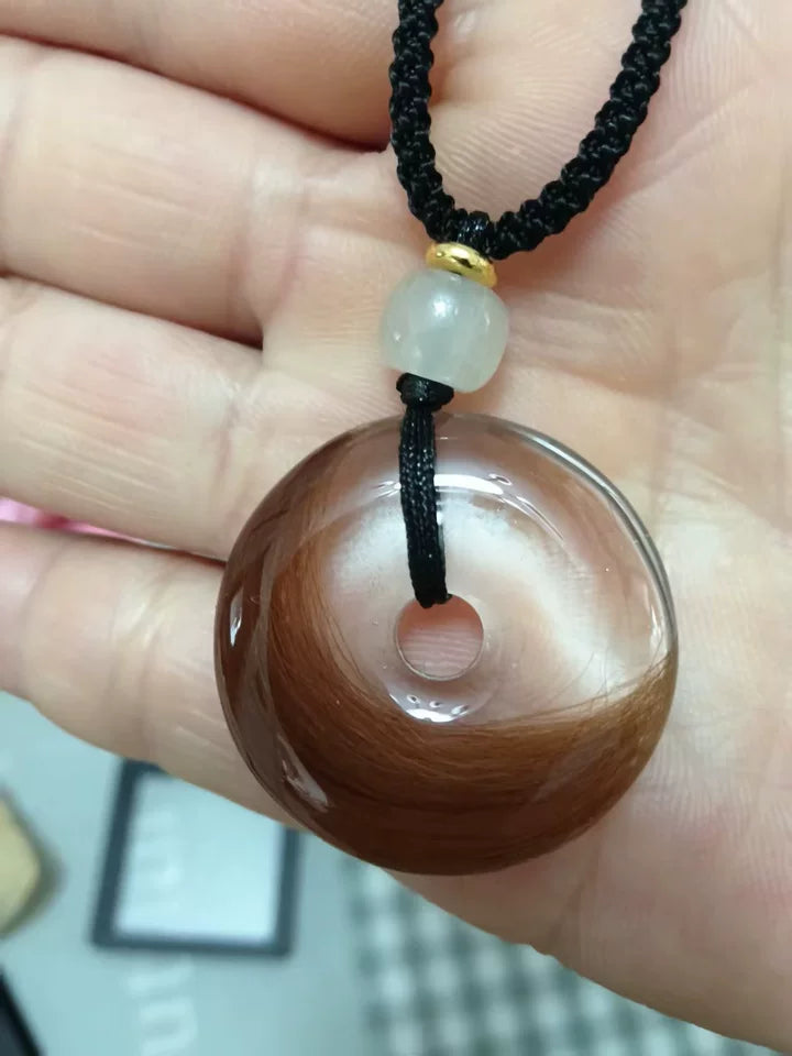 Hand holding a clear round pendant filled with warm brown pet fur