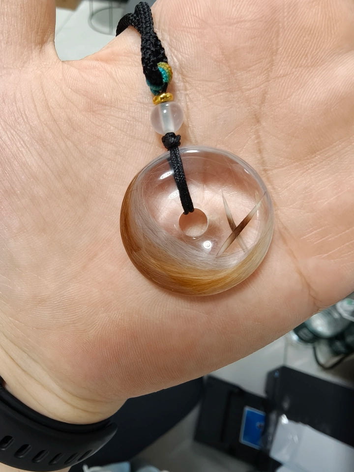 Hand holding a clear round pendant with naturally varied brown and white pet fur